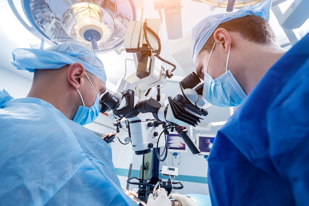 Two male Keck Medicine of USC experts in Alzheimer's disease and other neurological disorders look into a microscope in an operating room