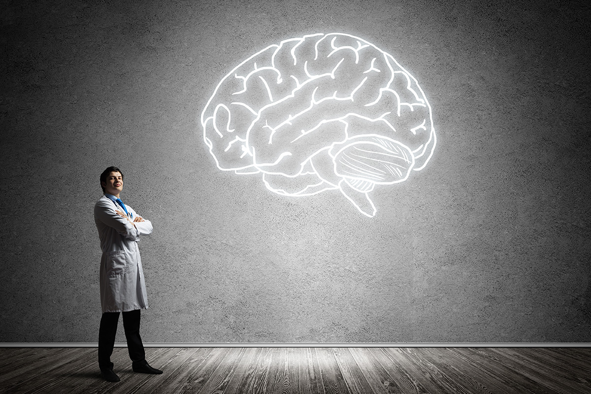 A Keck Medicine of USC brain aneurysm specialist stands cross-armed in front of a giant wall displaying a glowing white brain