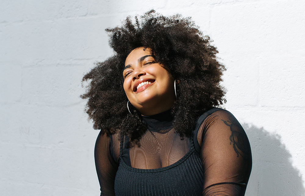 A woman smiles into the sun in a black shirt.