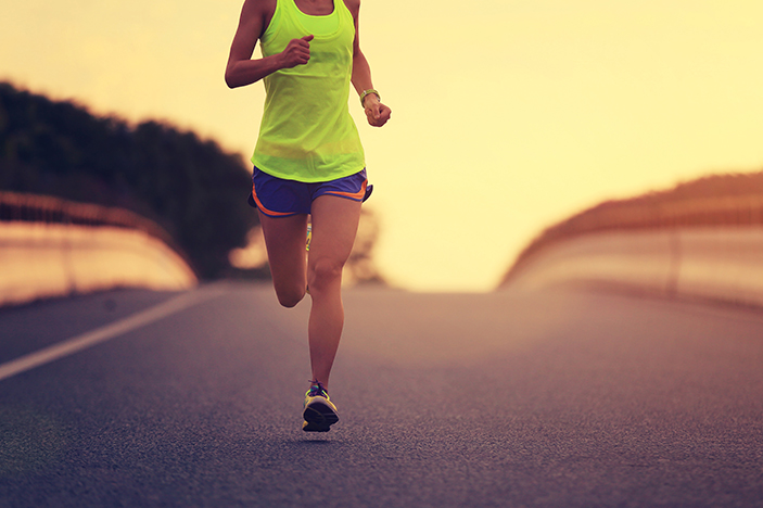 A woman runs on an empty road as the sun rises