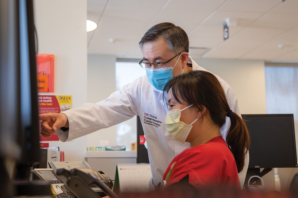 A Keck Medicine of USC physician in a surgical mask points at a medical scan as another masked medical staff person looks on