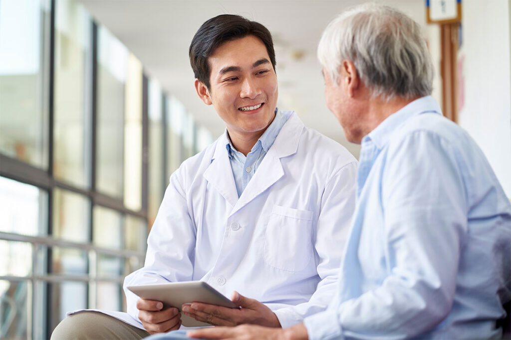 Friendly smiling asian doctor talking and explaining test result to elderly patient in hospital.