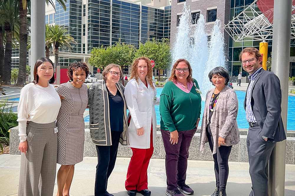 Several Keck Medical Center of USC physicians and nurse join liver transplant patient Benigna Carrillo in a smiling photograph outside Keck Hospital of USC