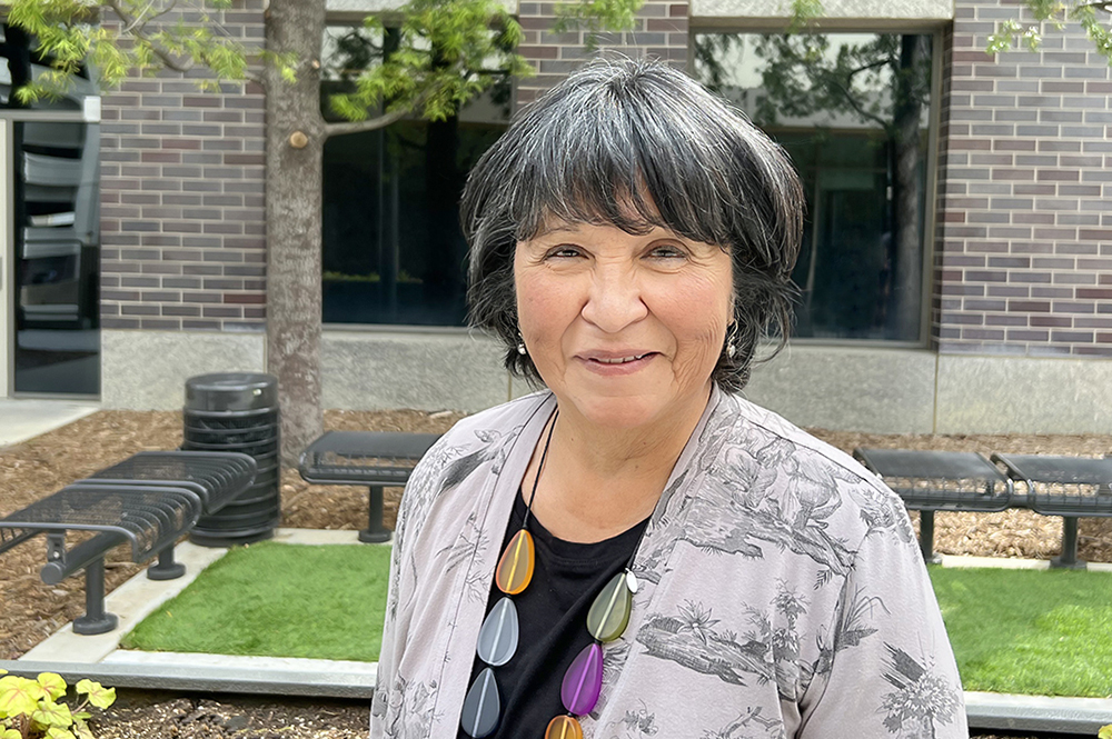 USC Liver Transplant patient Benigna Carrillo smiles in an outdoor portrait photograph in front of a green lawn and bench