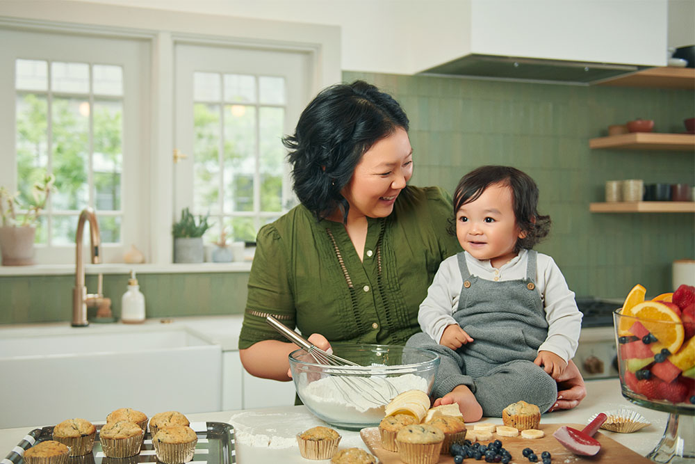 Melody LaTorre, a patient at the USC Brain Tumor Center, smiles with her toddler, who sits on top of a kitchen counter next to a stirred bowl of muffin mix