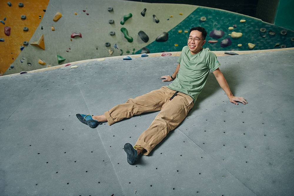 An Pham, a living-donor kidney transplant recipient, sits and smiles on the top of a climbing wall at a rock climbing gym