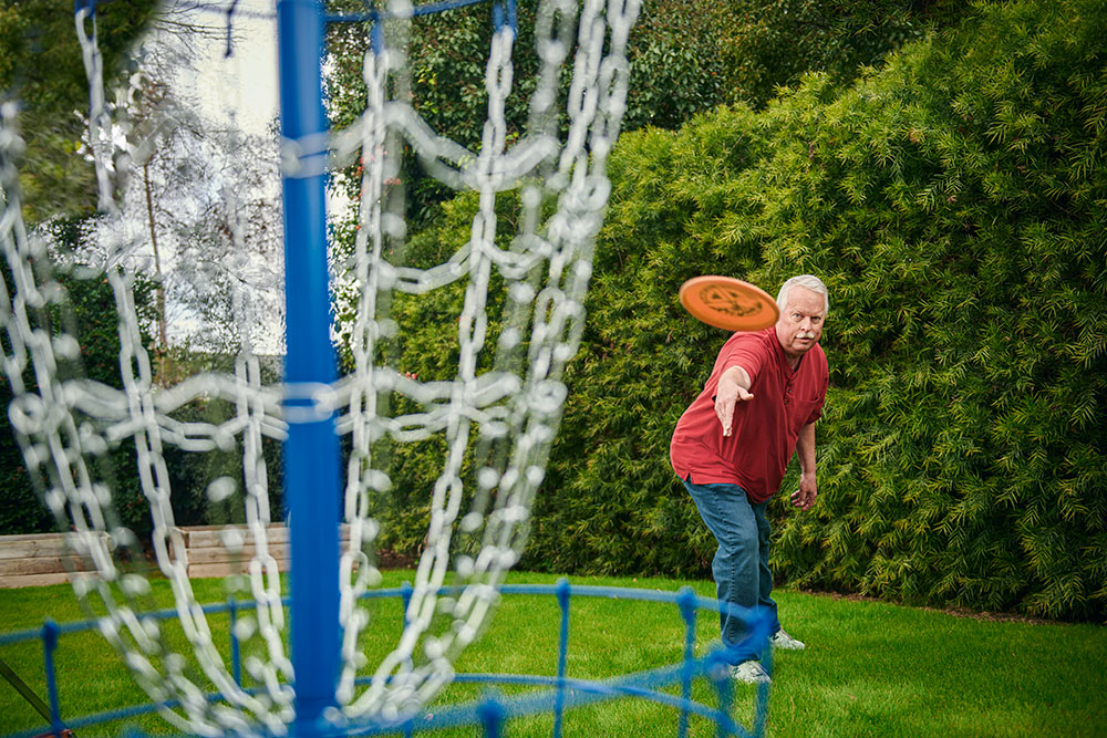 Roger Bignell, who received a triple bypass at USC Arcadia Hospital, throws an orange disc golf disc at a blue disc golf net