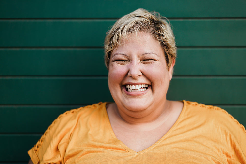 Portrait of a woman smiling outdoors with green background.