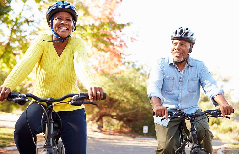 A woman and man smiling while riding their bikes in a park