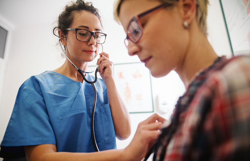 A female doctor checks a woman's heartbeat.