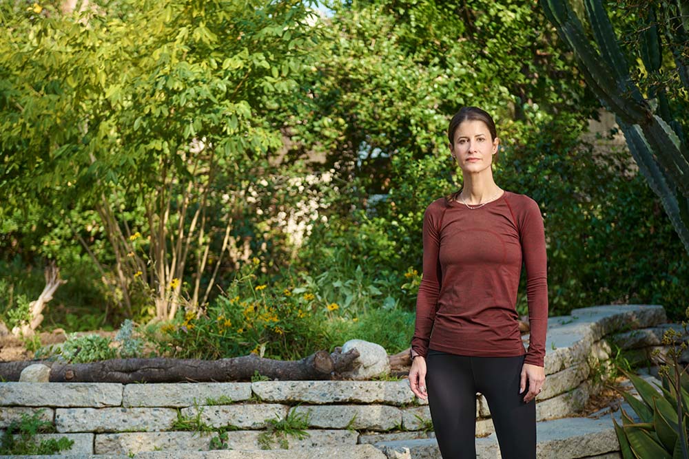 Triathlete Laura Brezin Kern stands in cardinal and black running attire in a garden setting