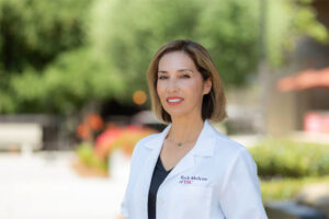 Dr. Lilyana Amezcua smiles while standing outside in a white medical coat.