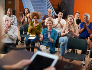 Group attending neighborhood meeting applauding speaker in a community center.