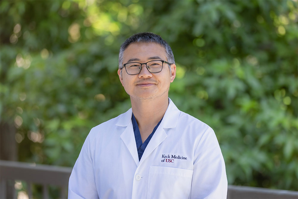 A portrait of Dr. Bing Zhang standing outside in a white medical coat.
