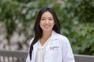A portrait of Sarah Kim outside with a white medical coat on.
