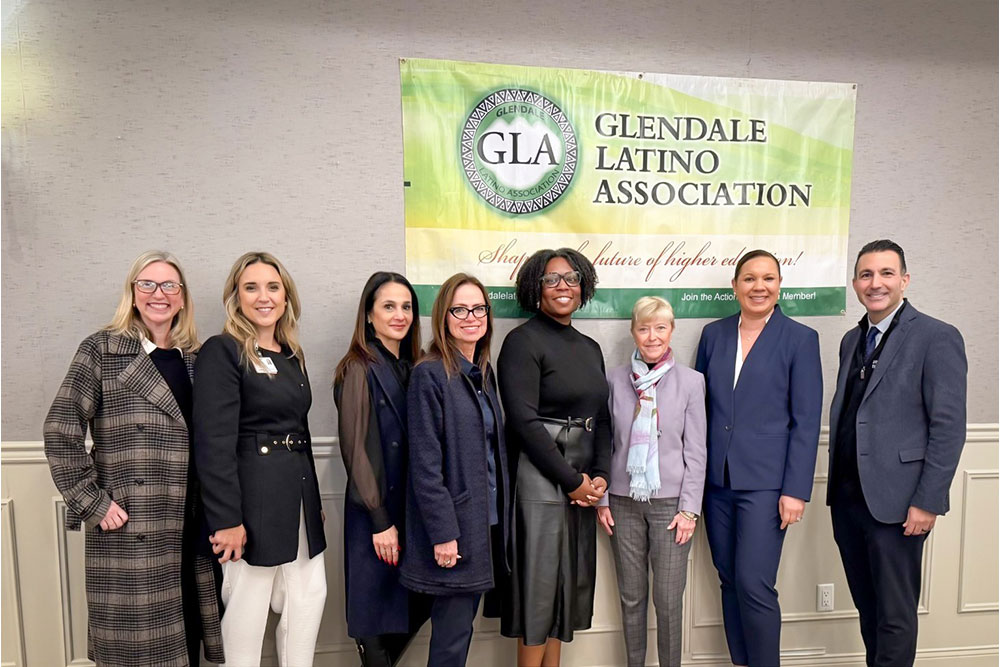 Group of smiling of women and a man in front of a banner that reads "Glendale Latino Association."