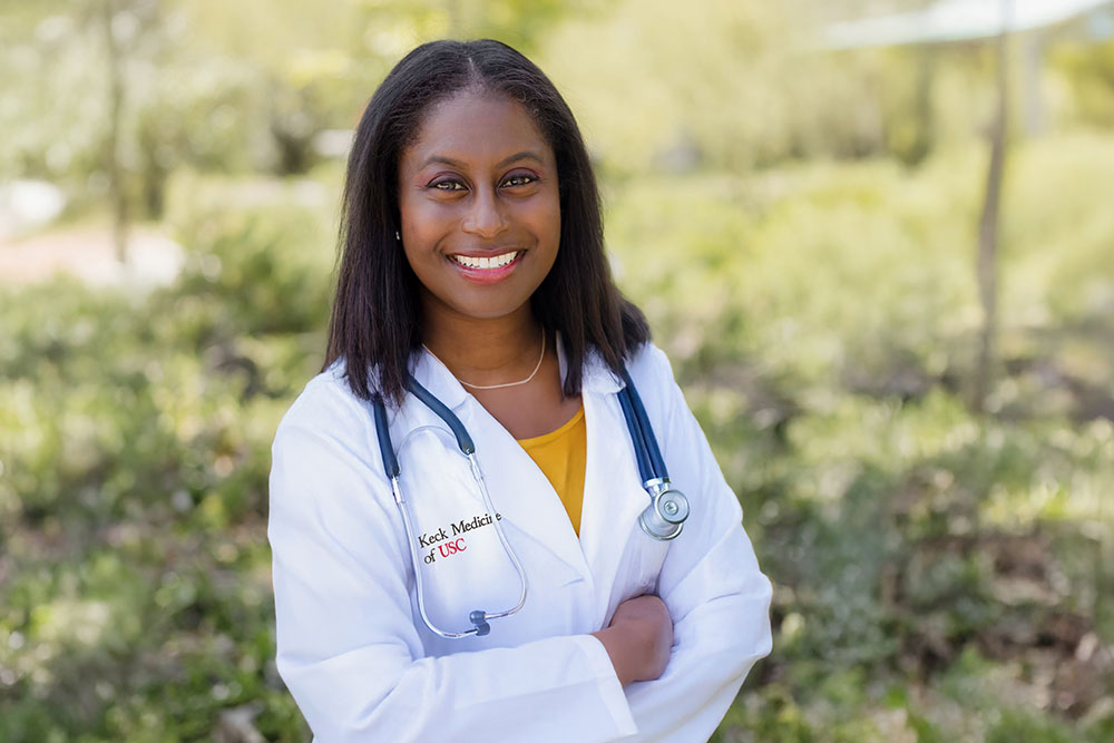 Dr. Florence-Damilola Odufalu stands outside and smiles while wearing a white medical coat.