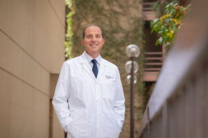 Dr. Saro Khemichian stands outside and smiles in a white medical coat.