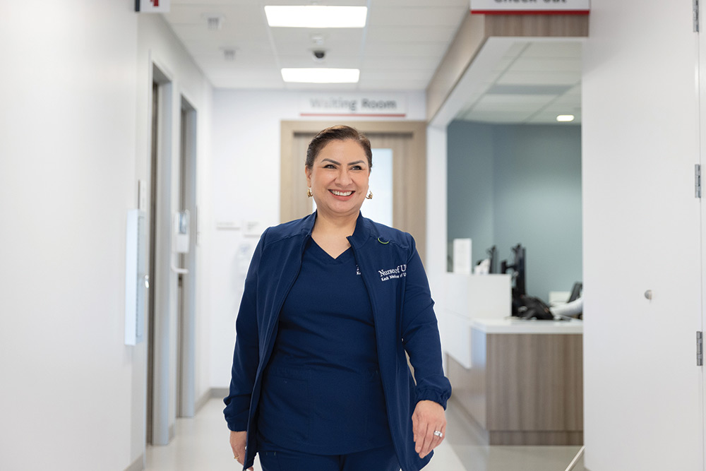 Luz Ahumada walks down the hallway of Keck Medicine - Pasadena's orthopedic surgery clinic wearing blue Keck Medicine scrubs and smiling