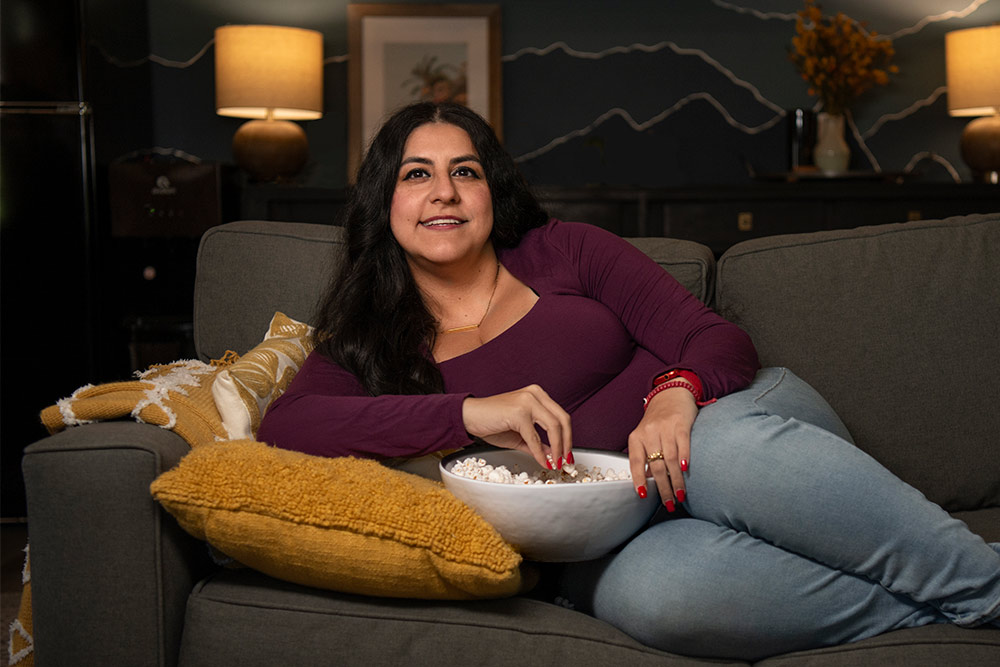 Sheila Rodriguez reclines on a couch with a bowl of popcorn