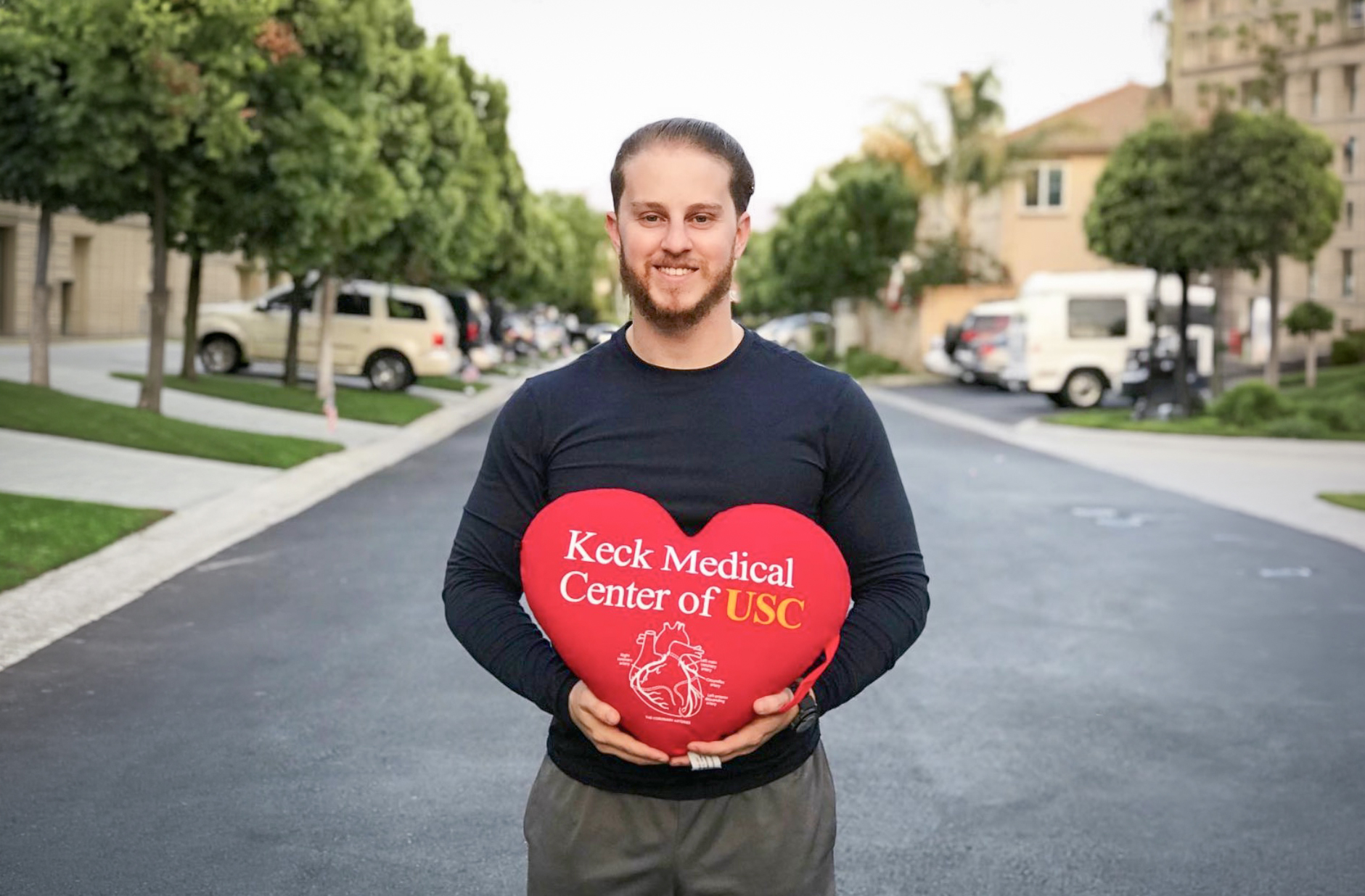 Keck Medicine of USC patient Arik Bibicoff standing on the street with a heart-shaped pillow that says Keck Medicine of USC.