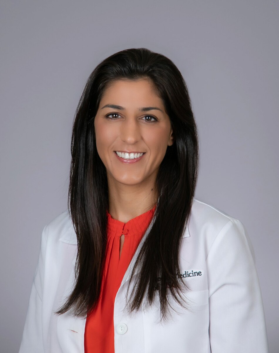 Dr. Moayer stands in a white medical coat against a grey background