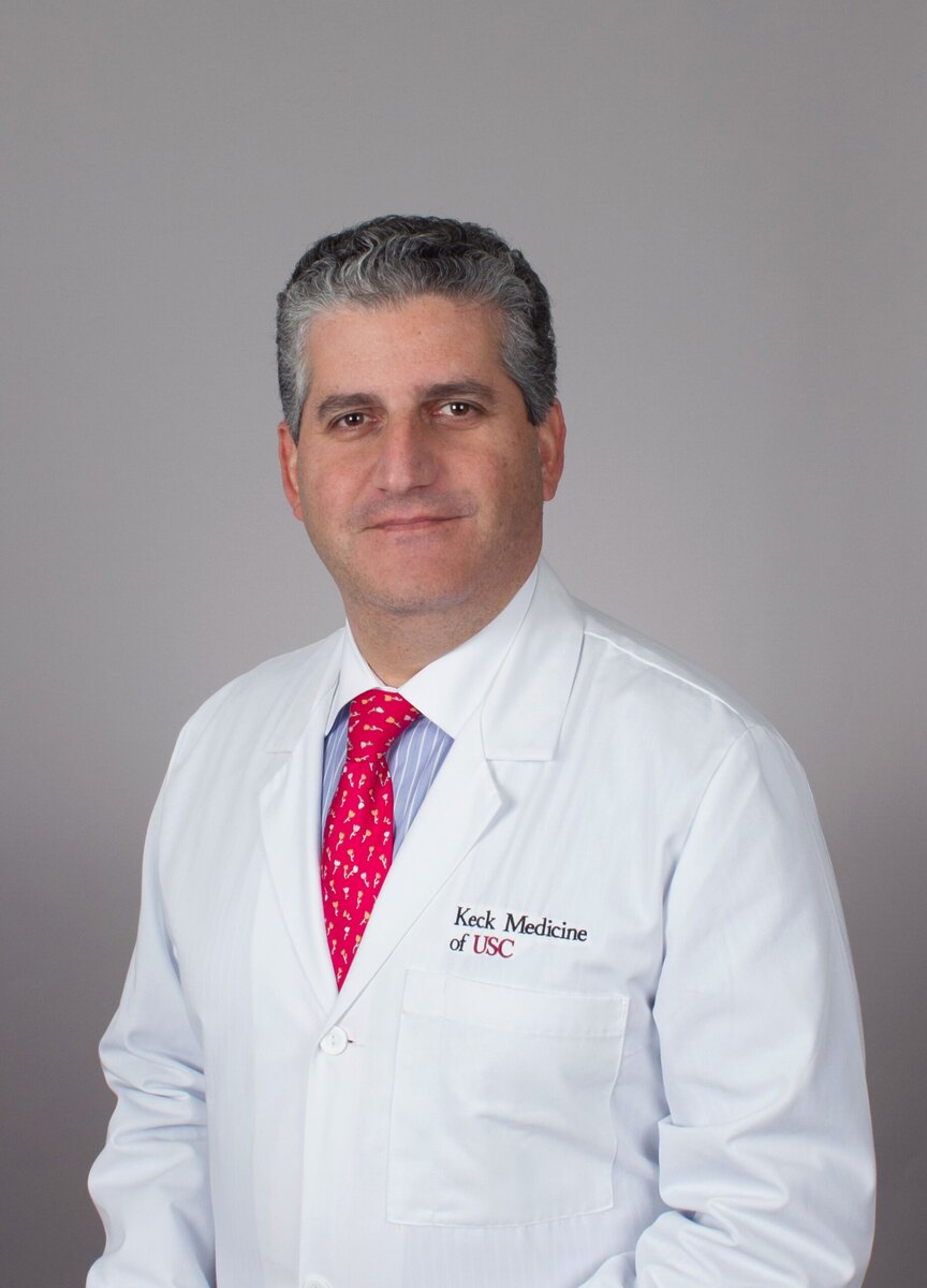 Dr. Fleischman stands smiling in a white medical coat against a grey background