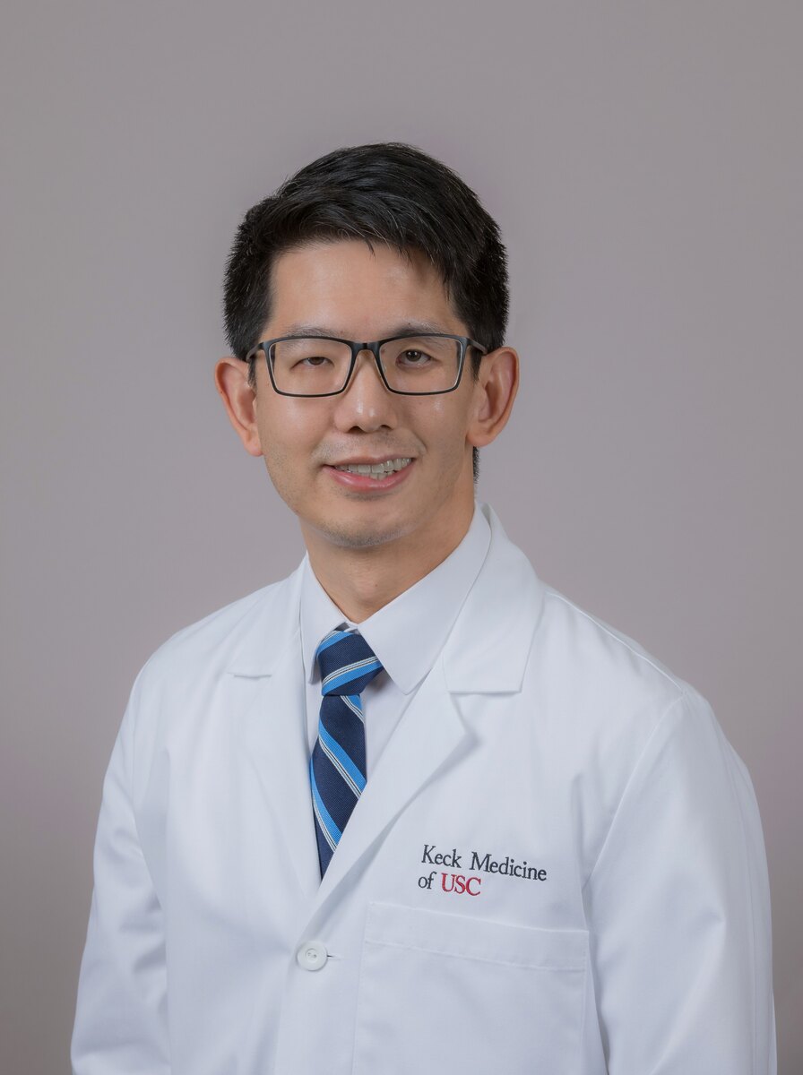 Dr. Hur stands against a grey background in a white medical coat.