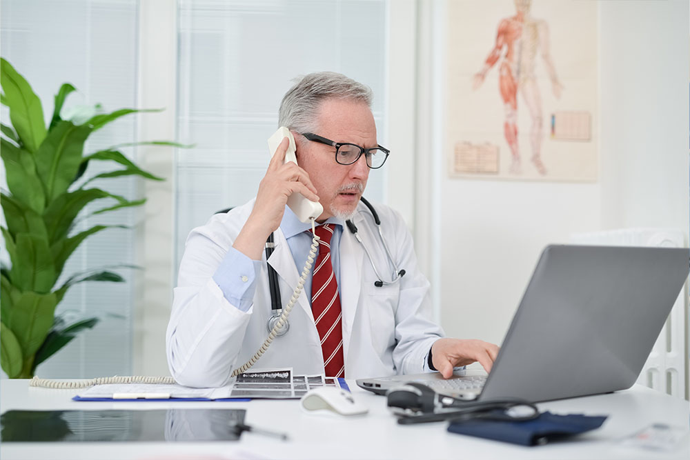 Community cardiologist on phone in office calls cardiac specialists.