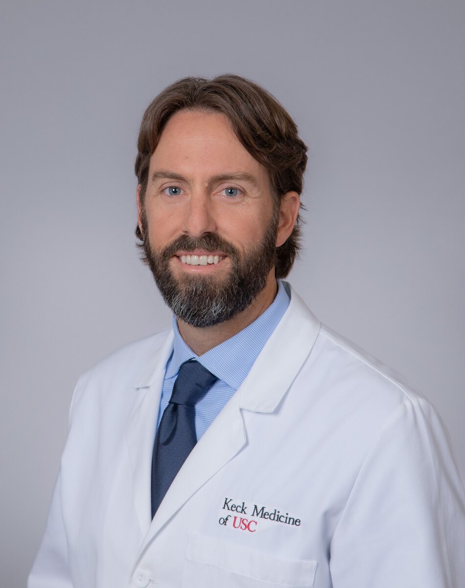 Dr. Putnam stands in a white medical coat, smiling against a grey background